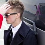 A man with sunglasses and a black coat adjusts his hair.