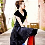 A woman in a black dress sitting outdoors on a bench.