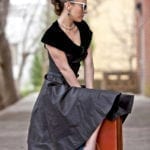 A woman in a vintage black dress sitting outdoors, looking to the side.