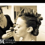 A woman getting makeup applied with her hair styled in rollers.