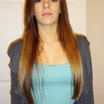 A woman with long brown hair wearing a blue top and gray sweater.