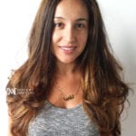 A smiling woman with long brown hair wearing a gray top.