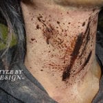 Close-up of a neck with brown paint splatters and streaks on the skin.