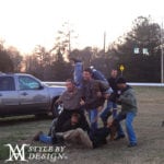 A group of six people posing playfully outdoors near vehicles at sunset.
