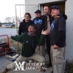 Five men posing outside a building, some smiling and gesturing.