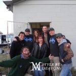 Group photo of eight people smiling outdoors in front of a building.