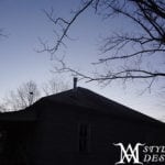 Silhouette of a house against a dusky sky with bare tree branches.