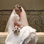 Bride in white dress holding a bouquet, sitting on a bench.