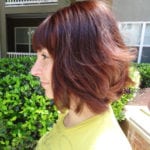 Profile of a woman with short reddish-brown hair outdoors.