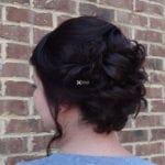 A woman with an elegant braided updo hairstyle standing against a brick wall.