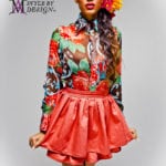 A colorful fashion model wearing a floral top and bright orange skirt.