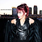 A woman with red hair wearing a black leather jacket against a city skyline.