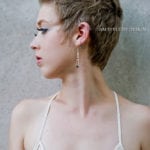 Profile of a woman with short hair and elegant earrings against a textured wall.