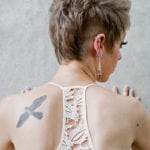 A person with a bird tattoo on their back, wearing a white lace top.