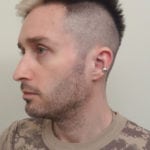 Side profile of a man with a short haircut and ear piercings.