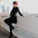 A stylish person posing on a rooftop with a city skyline in the background.