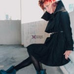 Person in a black dress sitting on a concrete ledge outdoors.