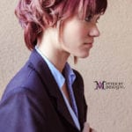 Profile of a person with short pink hair wearing a navy blazer.