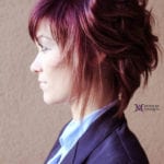 Side profile of a person with layered purple hair wearing a dark blazer.