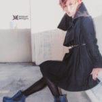 A person in a black coat and blue boots sitting outdoors.