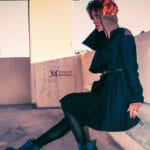 A person in a black outfit sitting on a concrete floor, covering their face.