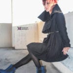 Person in black outfit and blue shoes sitting on stairs.