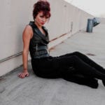 A woman in black sitting on a rooftop floor.