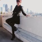A woman in black posing on a rooftop with a city skyline in the background.