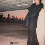 Person leaning against a pillar at sunset with a city skyline in the background.