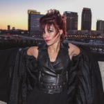 A woman in a black leather jacket with a city skyline at sunset.