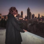Person in black coat overlooking a city skyline at dusk.