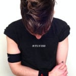 A person with brown hair looking down, wearing a black shirt with text.