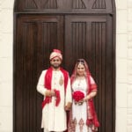 A couple in traditional attire standing in front of a wooden door.