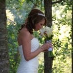 A bride in a white dress smelling a bouquet of white flowers.