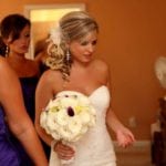Bride in white dress holding bouquet, assisted by bridesmaid.