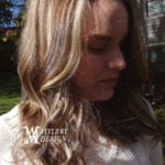 A woman with long, light brown hair and blonde highlights looking down outdoors.