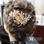 Intricate bridal hair updo with floral and pearl hair accessory.