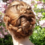 Intricately braided updo hairstyle on a woman with flowers in the background.