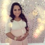 A pregnant woman in a white dress smiling and holding her belly.