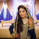 A bride in traditional attire posing indoors with elegant jewelry and makeup.
