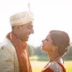 A couple in traditional attire smiling at each other outdoors.