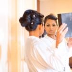 A woman in a white robe looking at herself in a mirror.