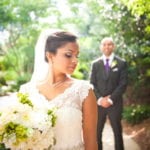 Bride in white dress with groom in background outdoors.