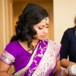 A woman in a purple sari looking down, adorned with traditional jewelry.