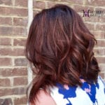 Woman with wavy brown hair against a brick wall.