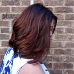 A woman with shoulder-length brown hair against a brick wall.