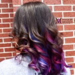 Curly hair with purple and blue highlights against a brick wall.