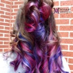 Long hair dyed with vibrant purple, blue, and pink hues against a brick wall.