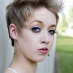 Close-up portrait of a young woman with short blonde hair and striking blue eye makeup.