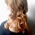Side view of wavy, blonde-highlighted hair over a tattooed shoulder.